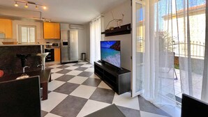 Una sala de estar moderna con un televisor grande, un piso a cuadros y una cocina al fondo.