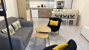 Una sala de estar moderna con un sofá gris, dos mesas redondas de madera y sillas negras con cojines amarillos.