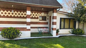 Una casa con fachada de ladrillo, un porche cubierto con sillas y un pequeño jardín.