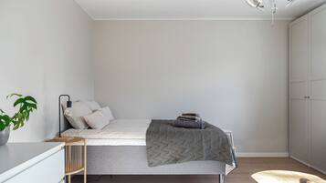 A minimalist bedroom with a bed, bedside table, lamp, and a potted plant.