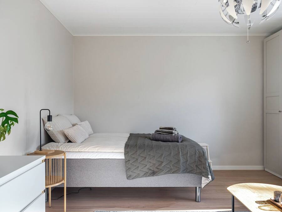 A minimalist bedroom with a bed, bedside table, lamp, and a potted plant.