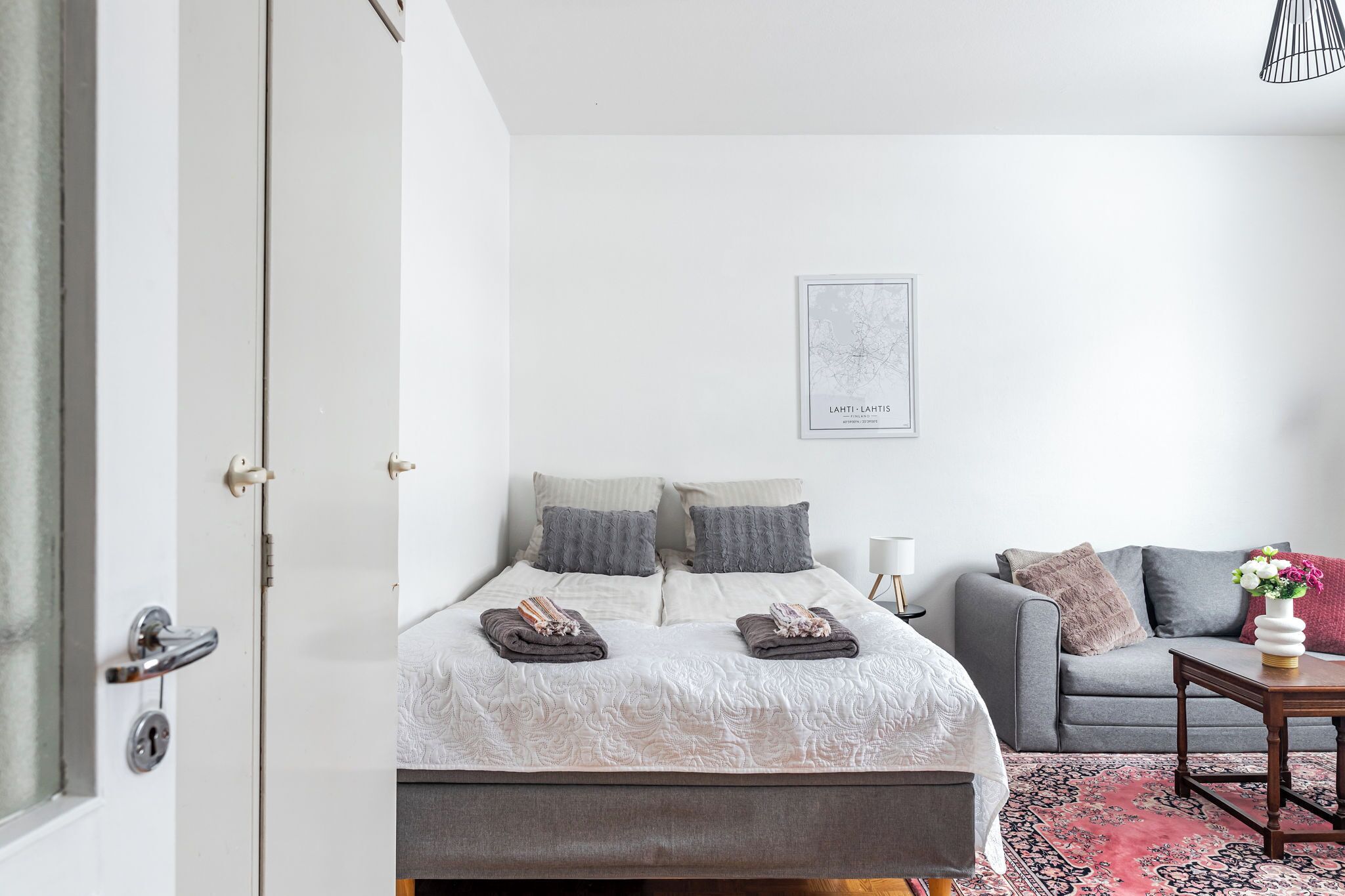 Un dormitorio con una cama, un sofá gris, una mesita y un cuadro en la pared.