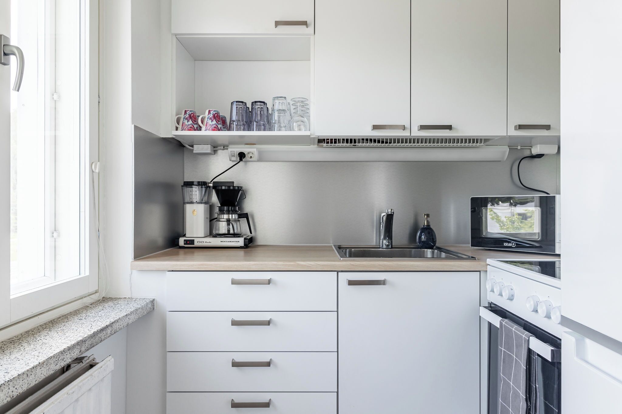 A modern kitchen with white cabinets, a coffee maker, a microwave, and a sink.