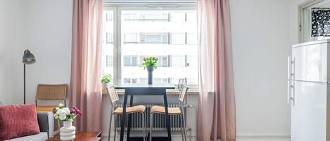 Un appartement moderne comprenant un coin repas, un canapé, une petite table avec un vase et une vue sur la ville grâce à de grandes fenêtres.