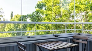 A balcony with a table and chairs, large windows, and a view of trees.