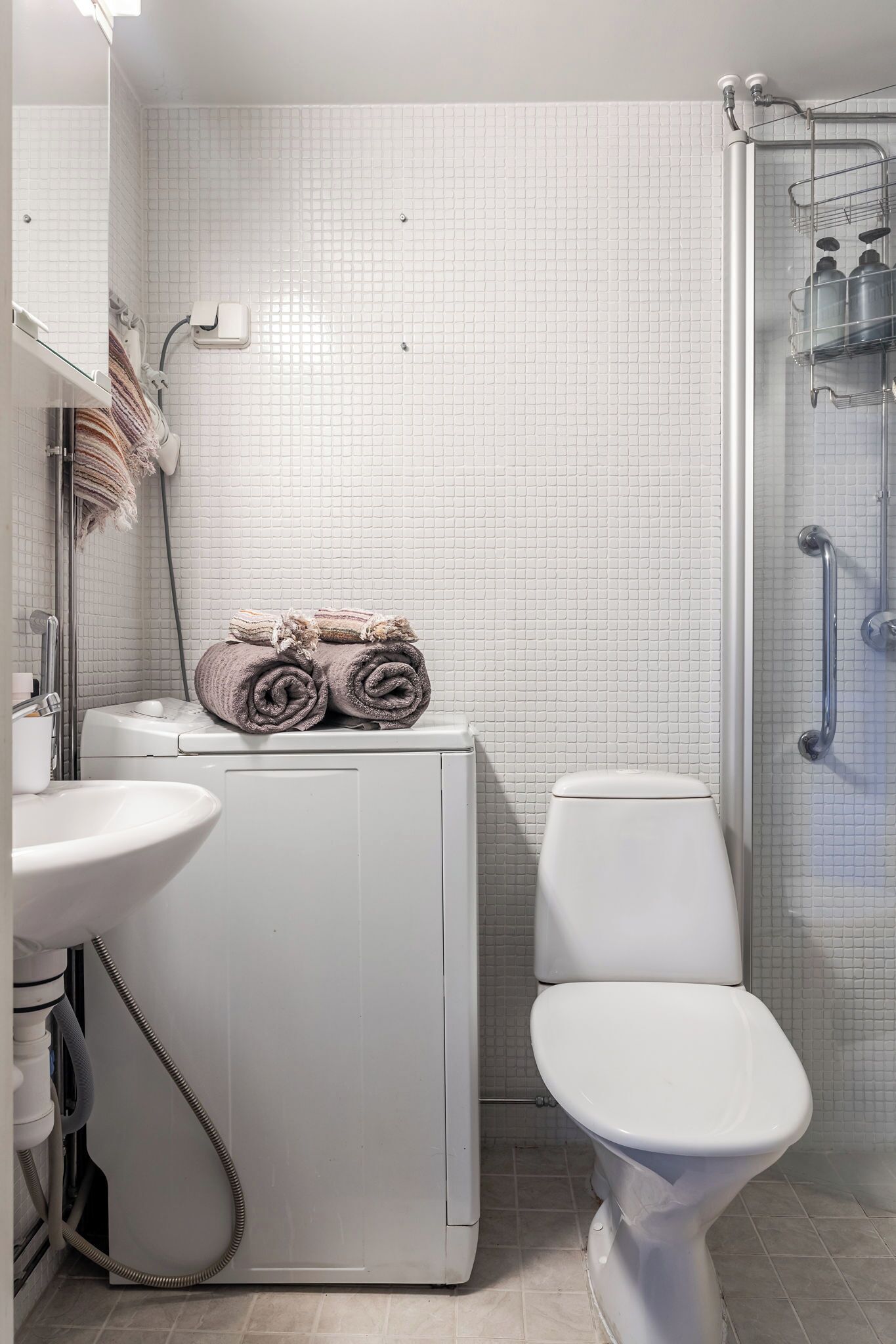 Un baño con inodoro blanco, lavamanos y zona de ducha con puerta de cristal.