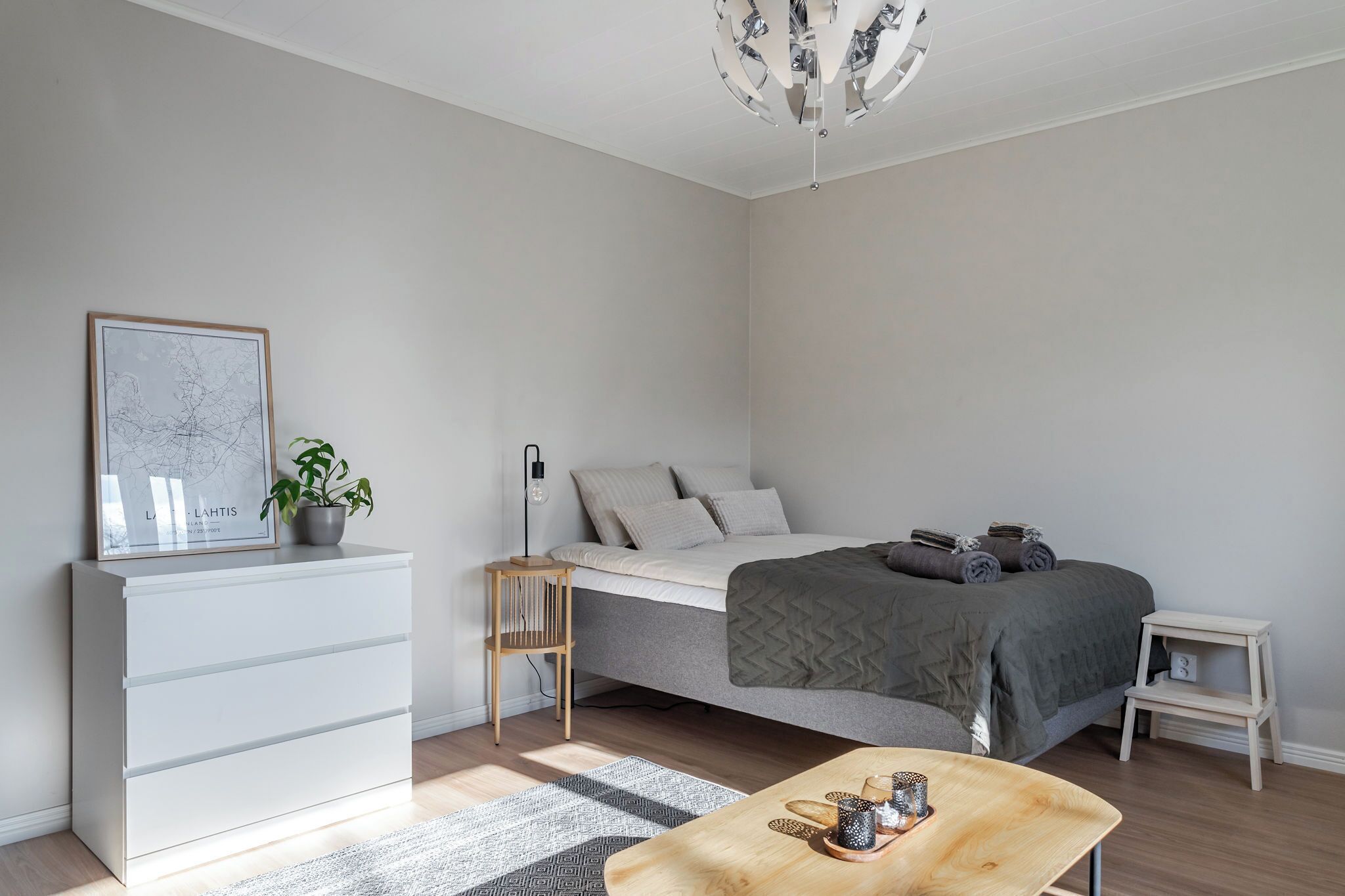 A minimalist bedroom with a bed, bedside table, nightstand, dresser, and a chandelier.