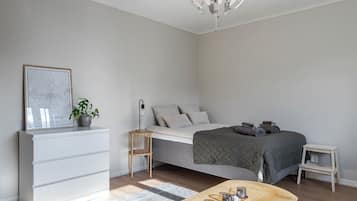 A minimalist bedroom with a bed, bedside table, nightstand, dresser, and a chandelier.