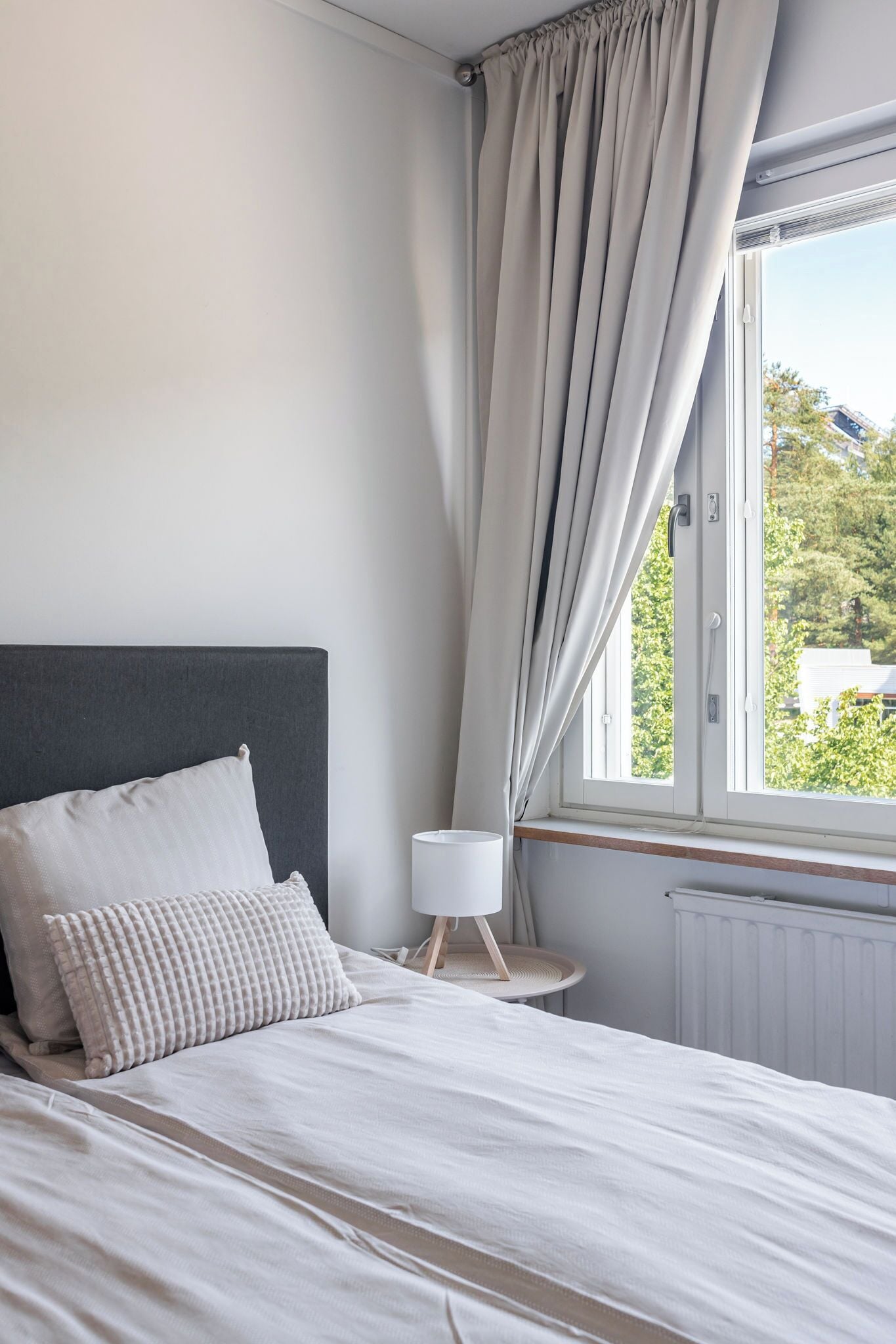 Un dormitorio con cama, mesita de noche, lámpara y ventana con cortinas.