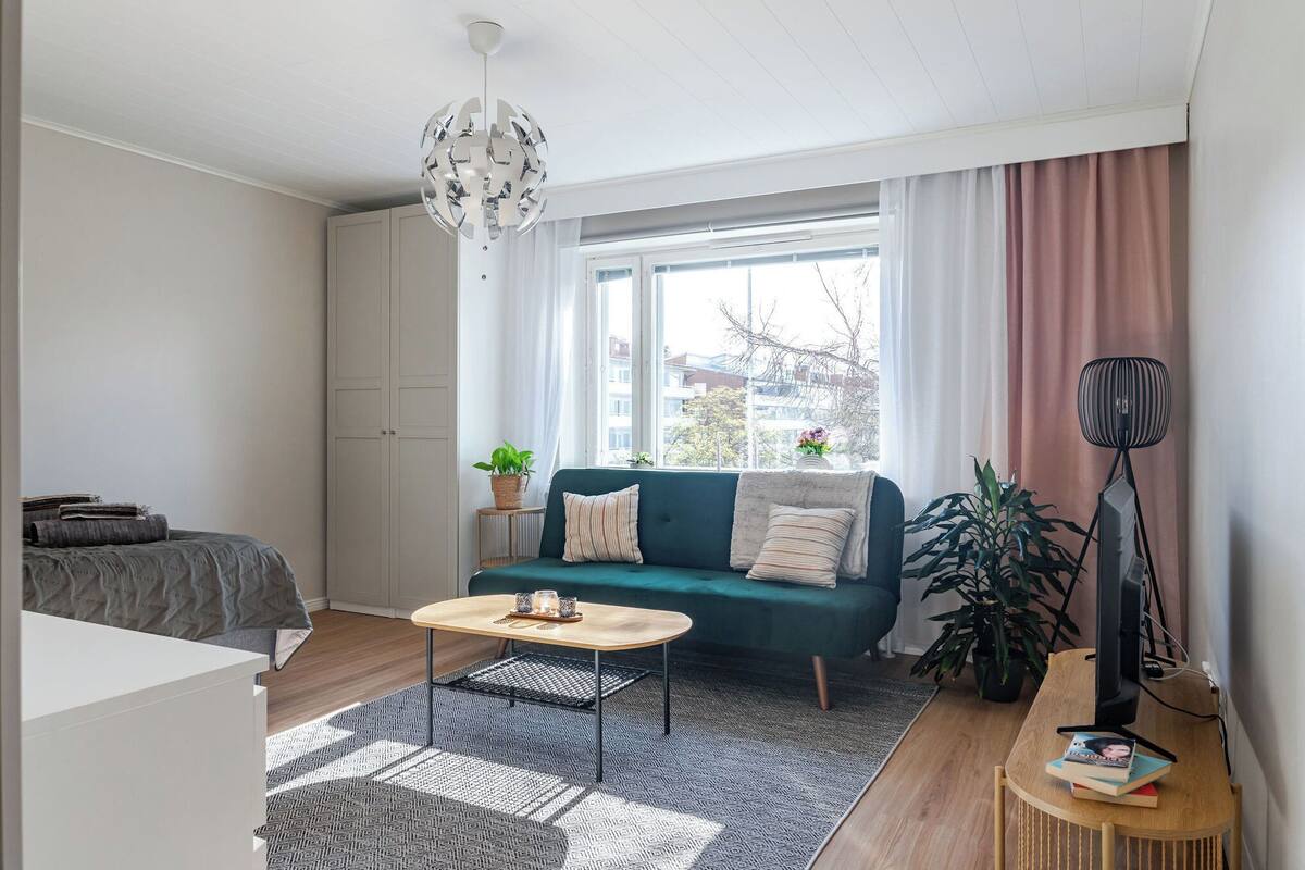 Un salon moderne avec un canapé vert, une table basse, un téléviseur et une grande fenêtre avec des rideaux.