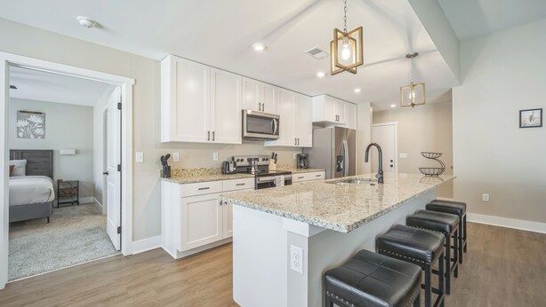 A modern kitchen with white cabinets, a granite countertop, and a central island with bar stools. - Traverse City Flats (Williamsburg)