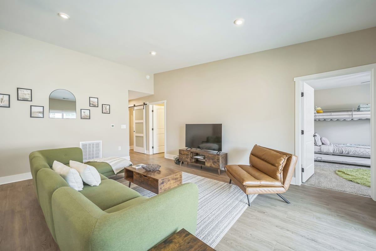 A modern living room with a green sofa, a brown leather chair, a wooden coffee table, and a flat-screen TV.