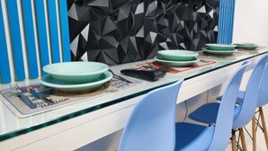 Een eethoek met een glazen tafel, blauwe stoelen en borden gedekt voor een maaltijd.