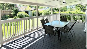 A covered patio with a table and chairs, white railings, and a view of a backyard with greenery and a shed. - Central 5-BR Retreat with Basement Kitchenette & Convenient Freeway Access (Westminster)