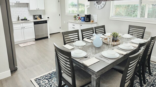 A modern kitchen with white cabinets, a dishwasher, and a dining area with a wooden table set for six. - Central 5-BR Retreat with Basement Kitchenette & Convenient Freeway Access (Westminster)