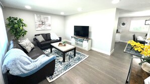 A modern living room with a sofa, coffee table, TV, and a dining area with a table and chairs. - Central 5-BR Retreat with Basement Kitchenette & Convenient Freeway Access (Westminster)