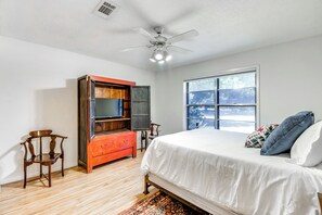 Un dormitorio con cama, ventilador de techo, ventana y cómoda de madera.