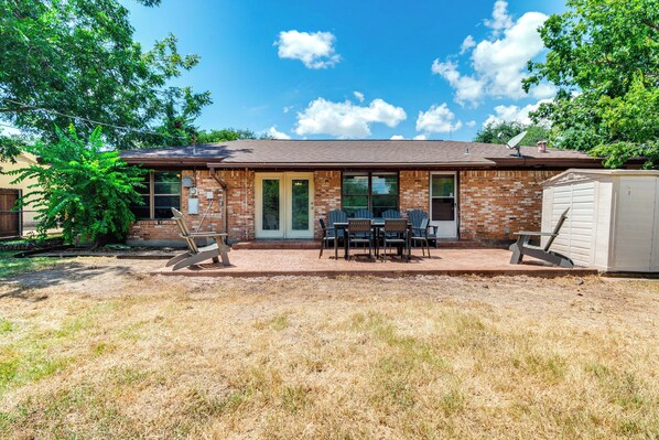 Una casa de ladrillo con patio, mobiliario exterior y un cobertizo.