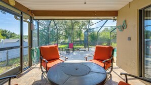 A covered patio with a round table and two orange chairs, overlooking a backyard with a pool and trees. - 5 Mi to Weeki Wachee: Spring Hill Home w/ Lanai (Spring Hill)