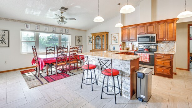 A spacious kitchen with wooden cabinets, a large island, and a dining area with a red table and chairs. - 5 Mi to Weeki Wachee: Spring Hill Home w/ Lanai (Spring Hill)