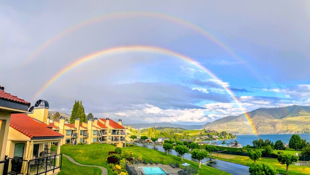 A resort with multiple buildings, a swimming pool, and a view of a lake and mountains.