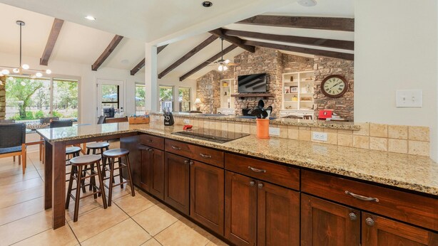 A spacious kitchen with a large island, dark wooden cabinets, and a stone accent wall. - Beautiful Pool home on 2.5 acres with a serene country feel with urban location (Round Rock)