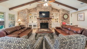 A living room with stone walls, a fireplace, leather sofas, and a television. - Beautiful Pool home on 2.5 acres with a serene country feel with urban location (Round Rock)