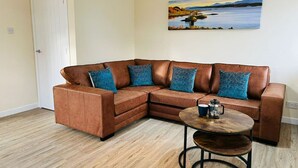 A living room with a brown leather sectional sofa, a round coffee table, and a painting of a landscape on the wall.