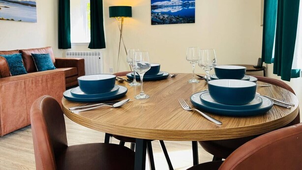 A dining area with a round wooden table set for four, blue dinnerware, and a painting of a night scene on the wall.