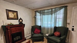 A living room with a fireplace, two armchairs, a framed map, and a door with a keypad lock. - Enjoy easy access to this  4 Bedroom smart home in downtown Hazleton PA.   (Hazleton)