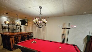 A pool table with a red felt surface, surrounded by a pool table frame. There are pool cues and a white cue ball on the table. - Enjoy easy access to this  4 Bedroom smart home in downtown Hazleton PA.   (Hazleton)