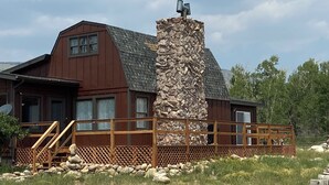 A rustic cabin with a stone chimney, wooden deck, and a view of the surrounding landscape.