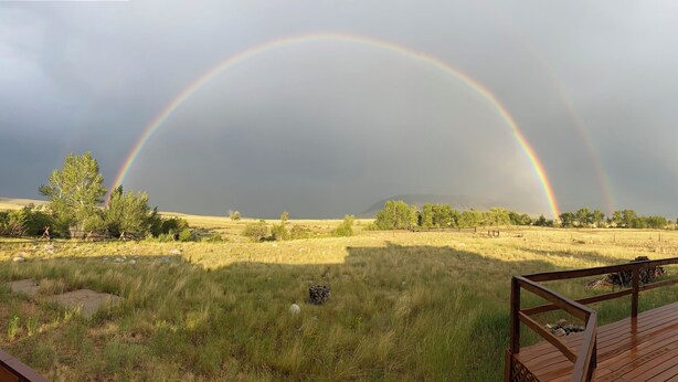 A wooden deck overlooking a grassy field with a rainbow in the distance.