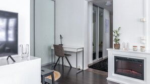 A modern living room with a flat-screen TV, a glass coffee table, a desk with a chair, a fireplace, and a potted plant. - Beautiful 1BR Apartment in Lahti Center (Lahti)