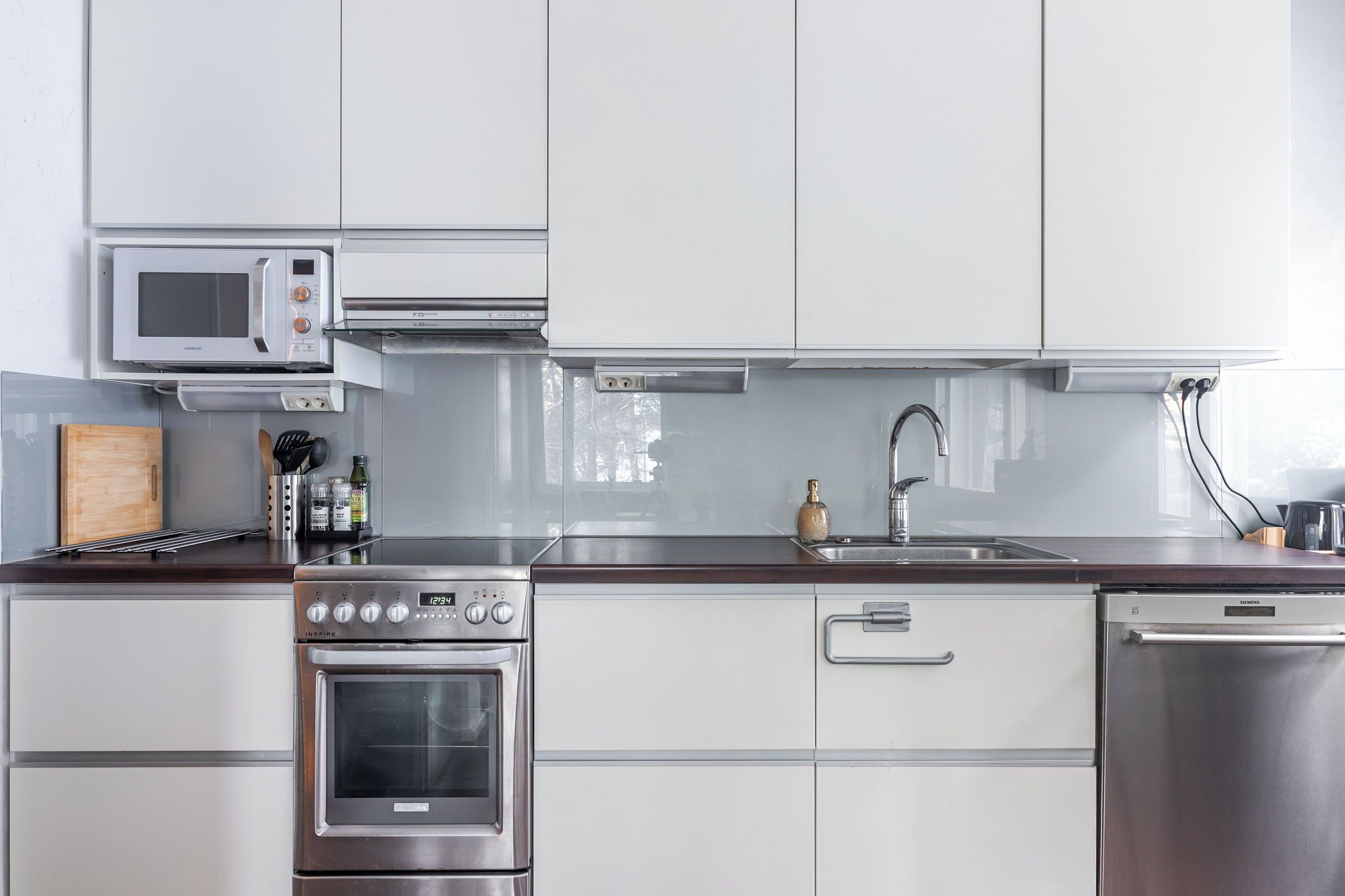 Una cocina moderna con armarios blancos, electrodomésticos de acero inoxidable, microondas, horno y lavavajillas.