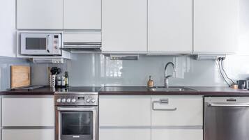 Una cocina moderna con armarios blancos, electrodomésticos de acero inoxidable, microondas, horno y lavavajillas.