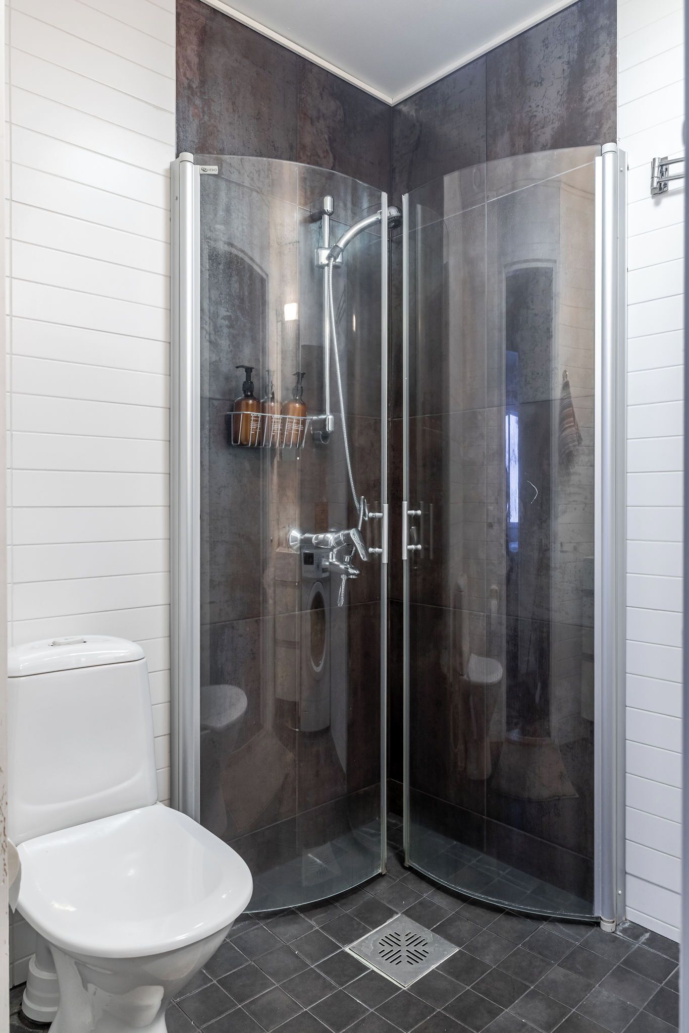 A corner shower with glass doors, a white toilet, and a tiled floor.