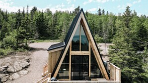 A wooden cabin with a triangular roof, large windows, and a gravel driveway. - Summit A-Frame (Two Harbors)