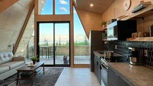 A modern kitchen with a large window, a dining area with a sofa, and a view of the outdoors. - Summit A-Frame (Two Harbors)
