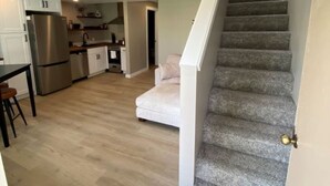 A modern kitchen with white cabinets and stainless steel appliances, a staircase with grey carpet, and a light wooden ceiling. - Crescent Bar Condo: On the river with Pool, Gorge shuttle/Wineries, AC (Quincy)