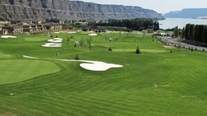 A golf course with bunkers, a clubhouse, and a view of a lake and mountains. - Crescent Bar Condo: On the river with Pool, Gorge shuttle/Wineries, AC (Quincy)