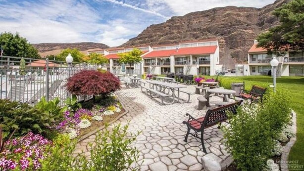 A hotel with a red-roofed building, outdoor seating area, and a mountainous backdrop. - Crescent Bar Condo: On the river with Pool, Gorge shuttle/Wineries, AC (Quincy)