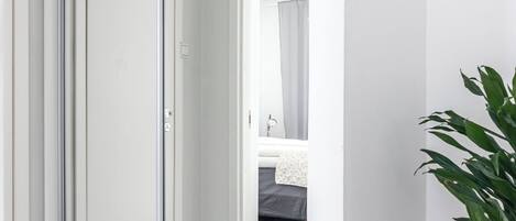 Ein modernes Hotelzimmer mit einer Schiebeglasdoor zum Balkon, einem kleinen runden Holztisch mit einer Pflanze und einem Bett mit weißem Kopfteil.