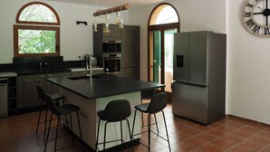 A modern kitchen with a central island, bar stools, stainless steel appliances, and a large wall clock. - "Villa Mammona 500m from Bonifacio harbour (Bonifacio)