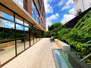 Een modern gebouw met grote glasramen, een houten terras en een tuin met planten en een waterpartij.