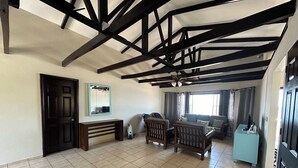 A spacious living area with a high ceiling, exposed beams, a large window, and a seating area with a sofa and chairs. - breath taken ocean views,  just 25 minutes away  from the airport.  (SAN LUIS TALPA)