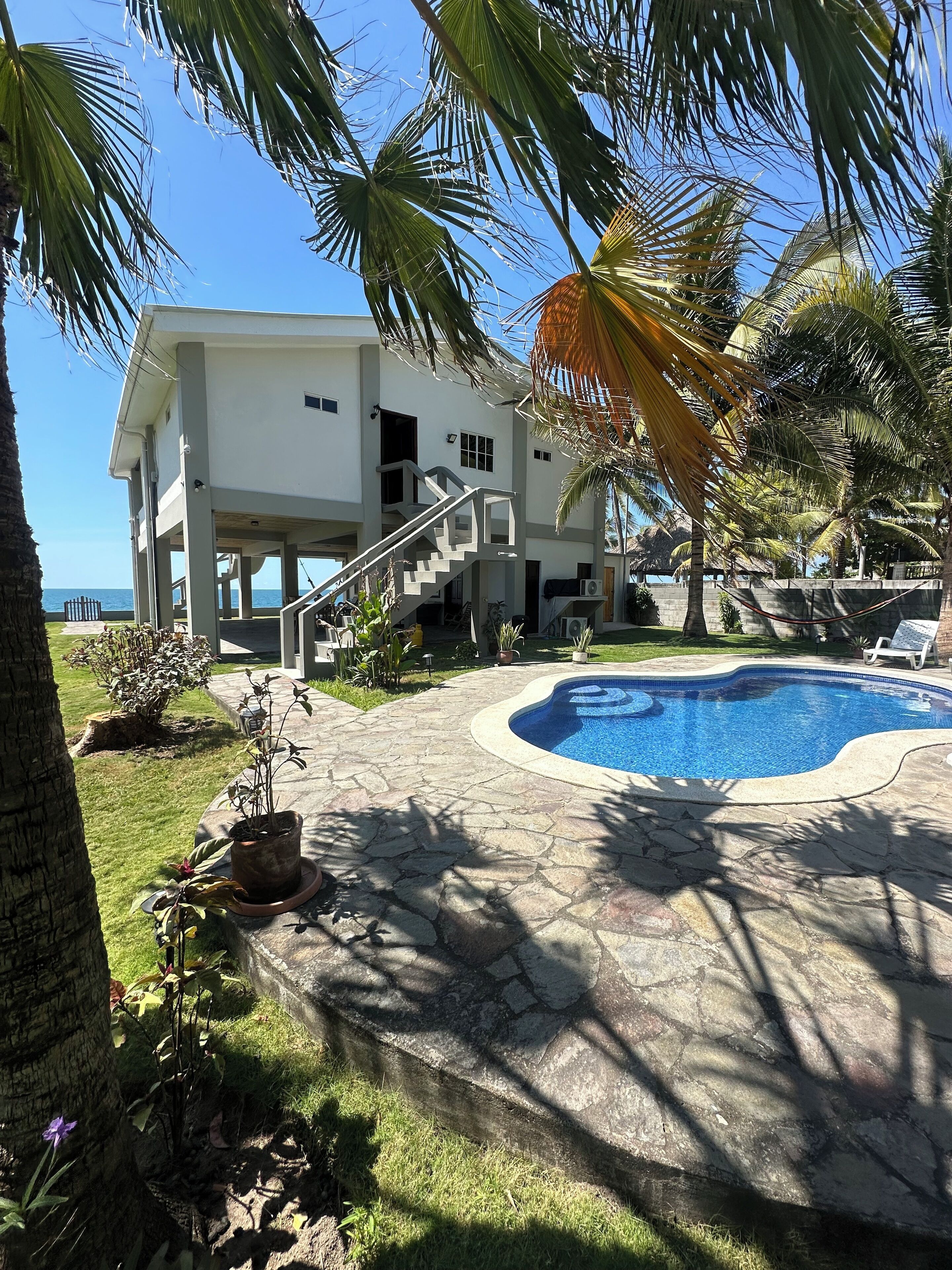 Una casa de dos pisos con piscina, rodeada de palmeras y vista al océano.