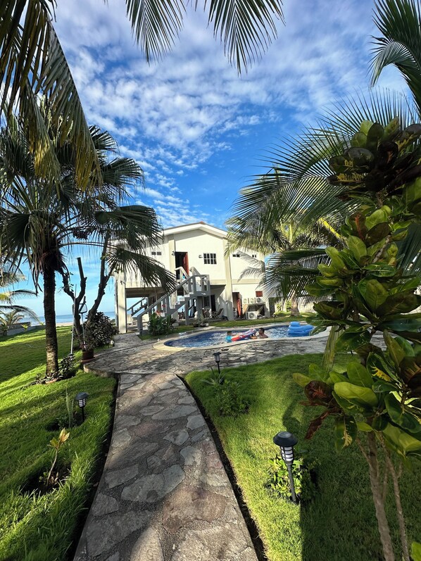 A pathway leading to a building with a pool, surrounded by palm trees and a clear sky. - breath taken ocean views, just 25 minutes away from the airport. (SAN LUIS TALPA)