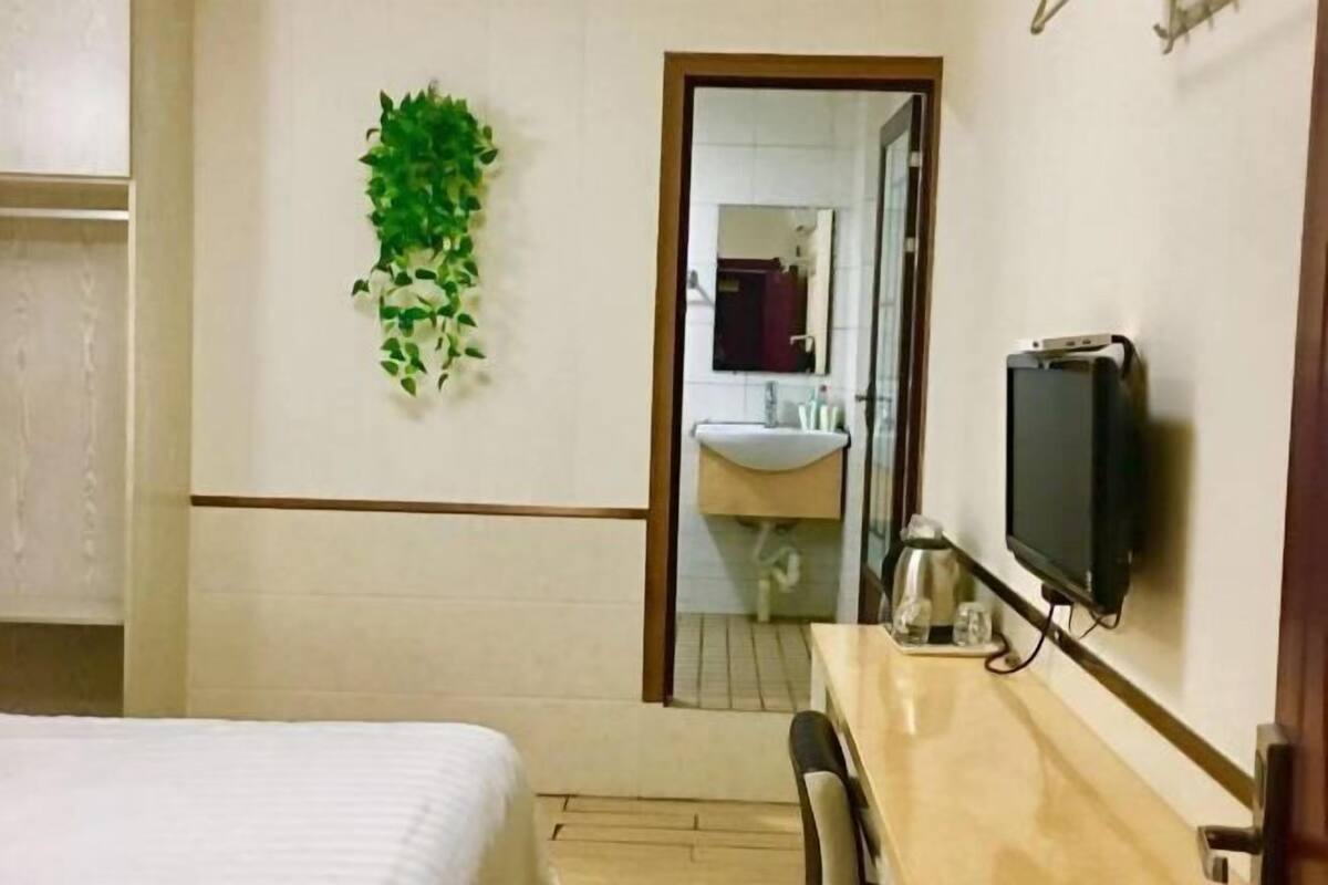 Une chambre d’hôtel avec un lit, un bureau avec une télévision, un miroir et une salle de bain visible à travers une porte ouverte.