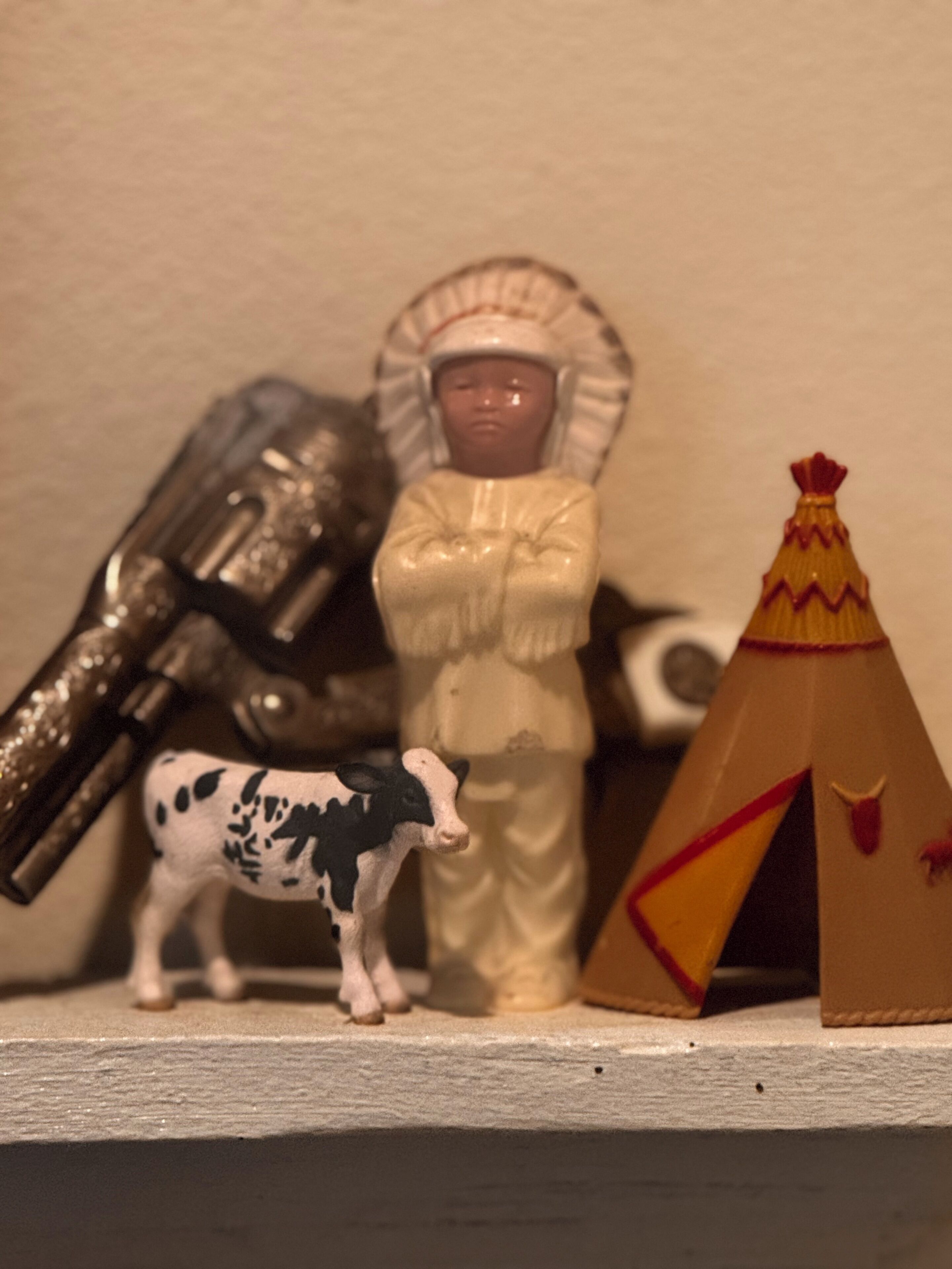 Una estantería con una figurita de una persona vestida de blanco, una vaca y una estructura tipo pirámide.